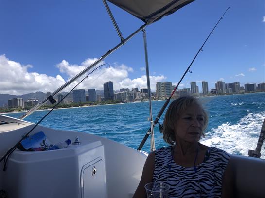 A woman relaxes on a boat as it moves through vibrant blue waters along a city beach.