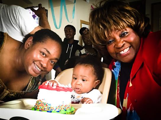 Family and friends gather to celebrate a baby's first birthday with cake and laughter.