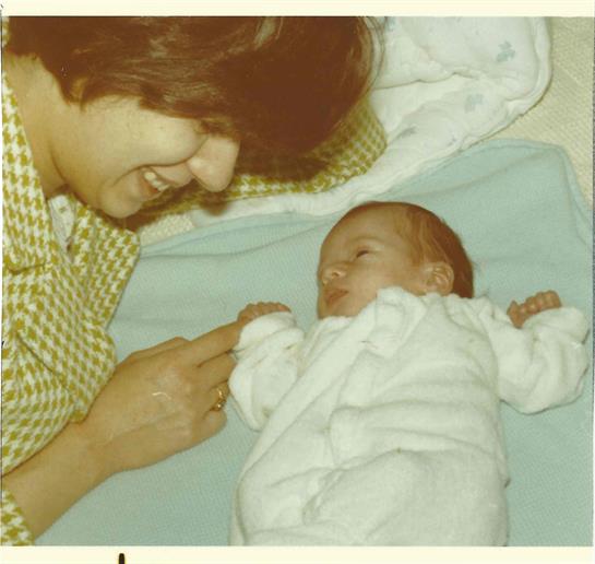 A mother smiles at her sleeping newborn baby while gently pointing at him.
