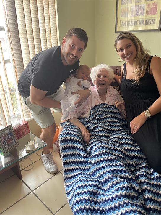 A loving family shares a warm moment in a sunlit living room with their grandmother and baby.