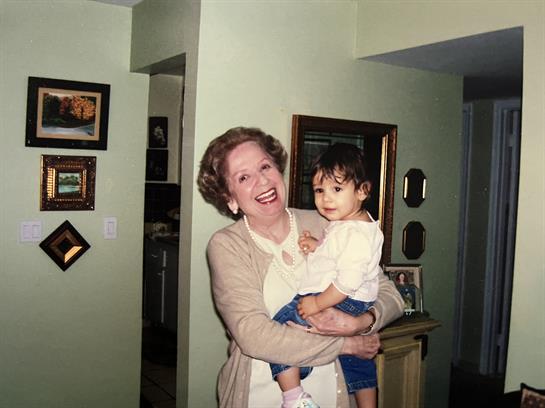 A grandmother holds her smiling granddaughter in a cozy, memory-filled living room.