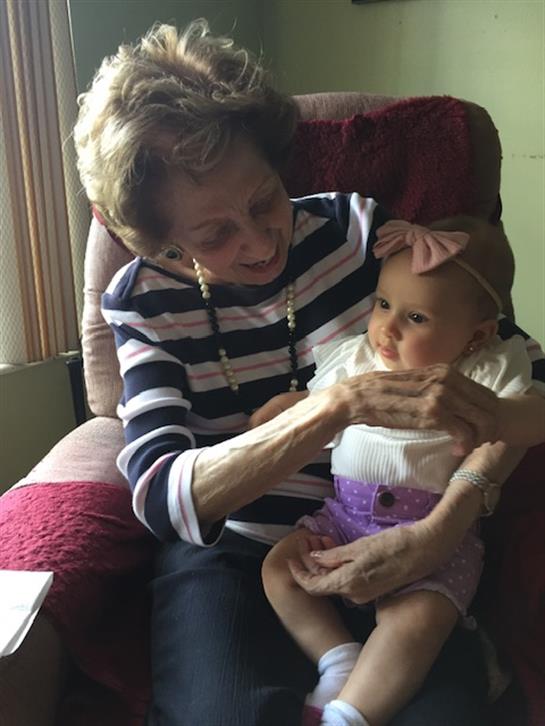 An elderly woman engages with her baby granddaughter, both smiling warmly, in a nostalgic setting.