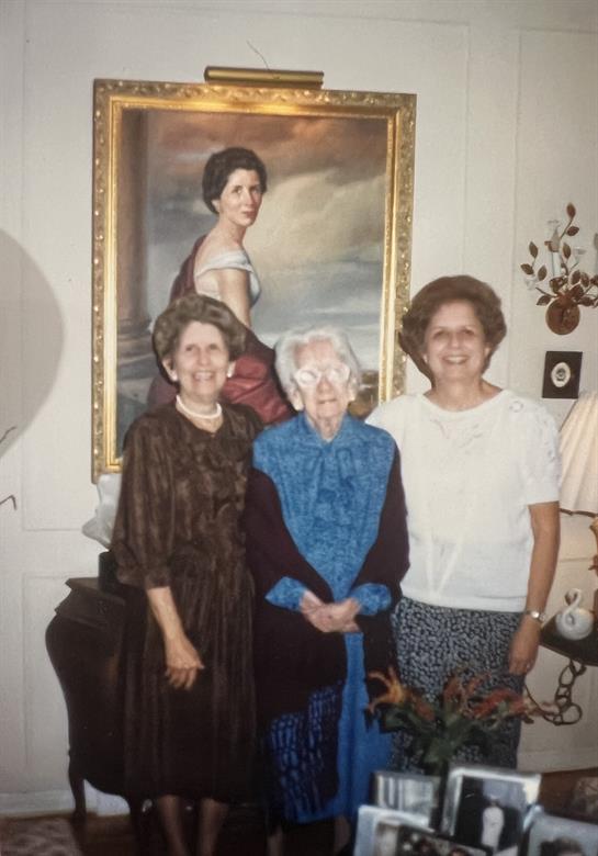 Three women pose together in a living room, showcasing family ties and history.