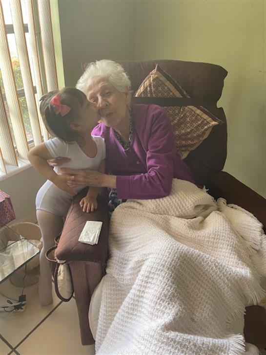 A young child lovingly embraces an elderly woman while sitting together in a bright living room.
