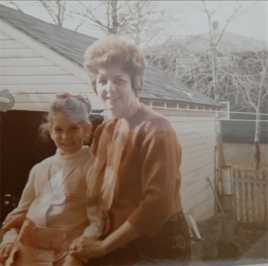 A woman and a young girl enjoy a sunny day in a backyard surrounded by trees.