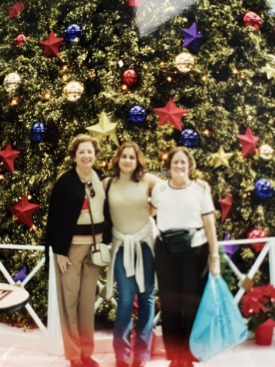 Three friends pose by a decorated Christmas tree, celebrating the holiday spirit.