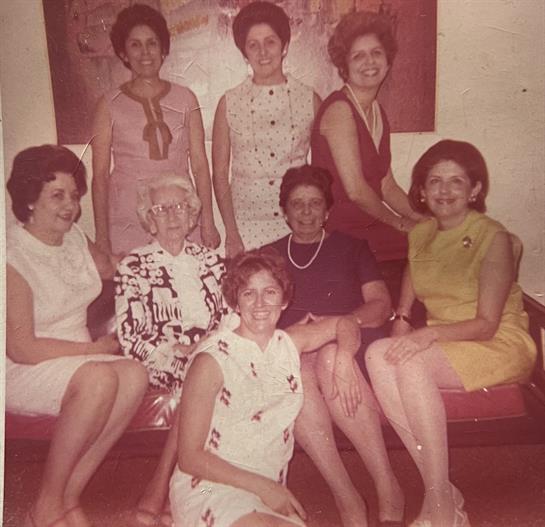 A group of eight women enjoys each other's company in a bright, inviting room filled with laughter.