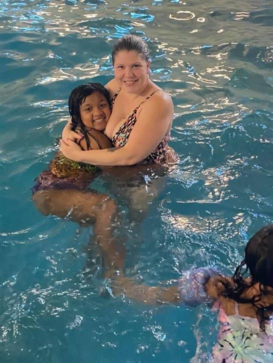 A woman holds her daughter in a warm, inviting swimming pool, both smiling joyfully.
