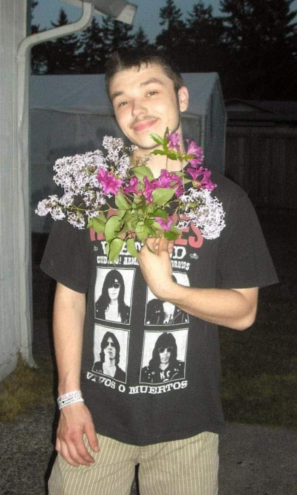 A man stands outside, smiling while holding a bouquet of vibrant flowers during dusk.