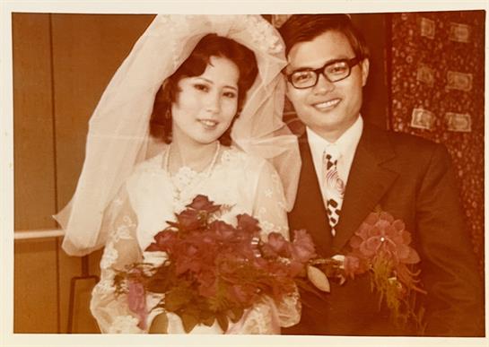 Newlyweds pose for a portrait, holding floral bouquets and smiling joyfully in formal attire.