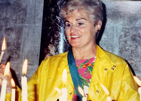 A woman in a vibrant yellow outfit lights candles in a calm temple atmosphere, smiling gently.
