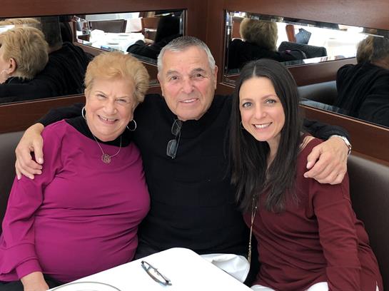 Three family members share smiles and laughter during a meal in a warm restaurant atmosphere.
