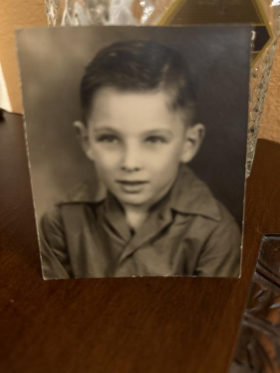 A young boy dressed in a vintage outfit poses for a formal portrait, showcasing a classic hairstyle.