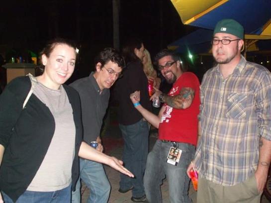 Four friends pose playfully outdoors at a carnival during the evening.