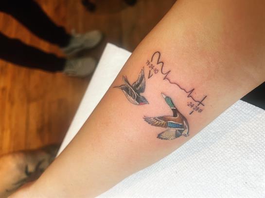A detailed tattoo of flying birds adorns a person's forearm inside a tattoo studio.