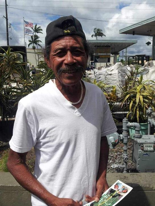 An elderly man stands outside with a friendly smile, holding a colorful flyer in his hands.