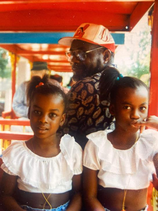 Children smile while standing with an older man in colorful surroundings, capturing joyful moments.