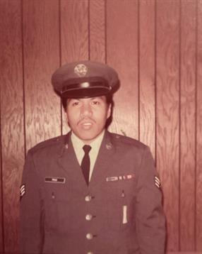 A serviceman stands proudly in full military uniform, displaying badges and insignia.