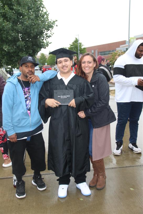 A graduate proudly poses with family members on a rainy graduation day, surrounded by supporters.