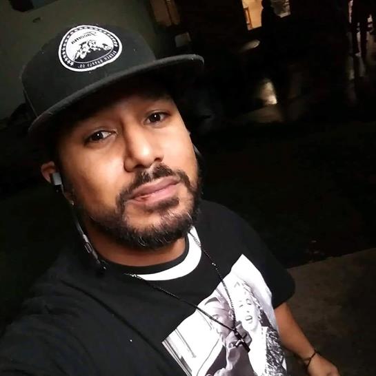 A man with a beard is smiling while taking a selfie indoors during evening hours.