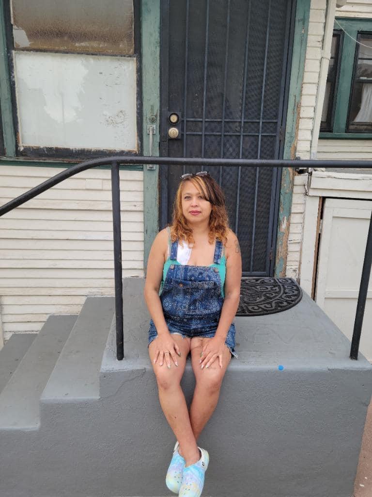 A woman relaxes on the steps of a house, absorbing the warm afternoon light while sitting casually.
