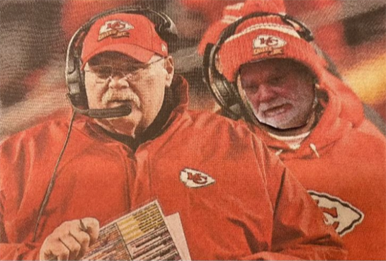 Coaches are discussing tactics while wearing winter gear in a chilly stadium atmosphere.