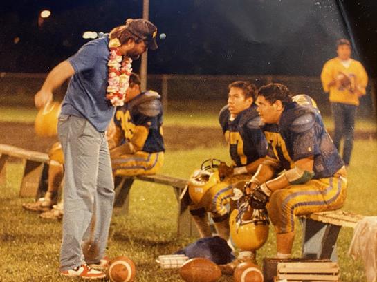 Coach motivates players while they rest on benches during an evening training session.
