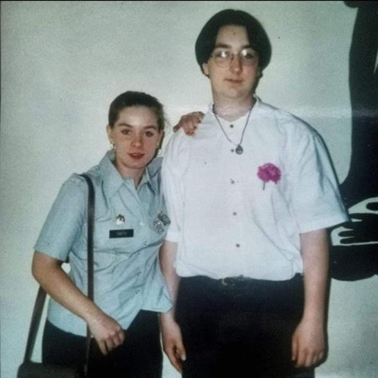 Two people smile together at a celebration, one in uniform and the other with a flower.