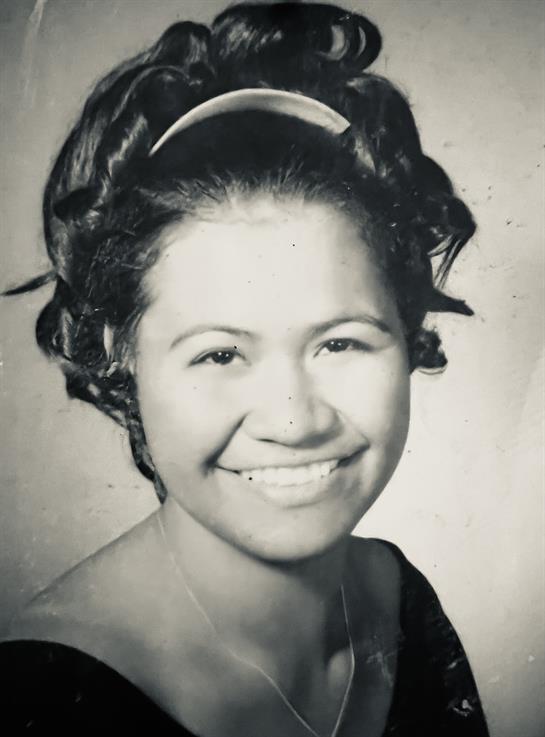 A young woman displays a bright smile, showcasing her curly hairstyle while wearing a formal dress.