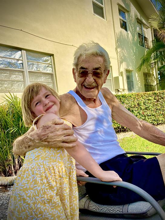 A joyful interaction takes place between an elderly man and a young girl outside in warm weather.