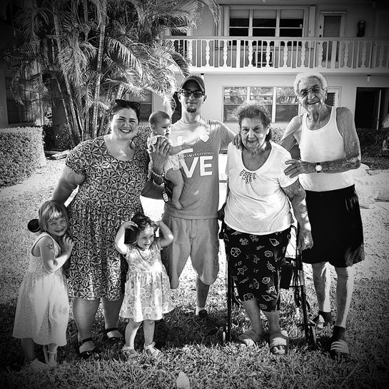 A multigenerational family poses happily outdoors on a sunny day in their lush backyard.