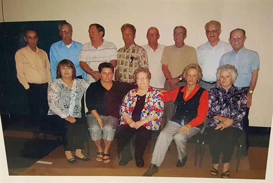 A cheerful group of twelve people poses together in a community hall for a special occasion.