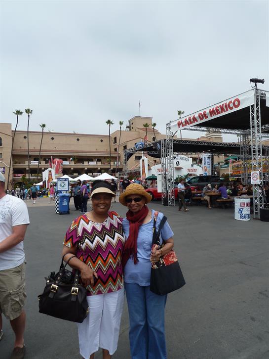 Two women smile as they pose together at a lively market in Plaza de Mexico, surrounded by stalls.