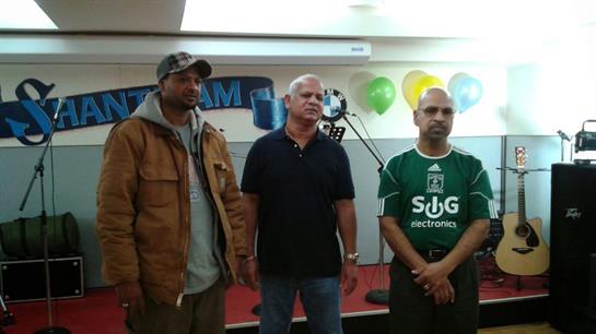Three men stand together in a community center, engaging in conversation during an event.