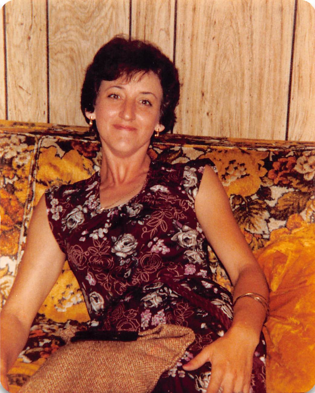 A woman sits comfortably on a plush, floral couch, enjoying her leisure time in a retro environment.