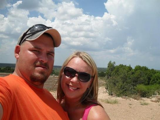 Couple smiles for a selfie while spending time outdoors on a sunny day with lush nature nearby.