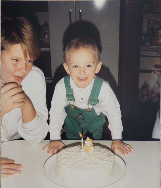 Two kids celebrate joyfully around a birthday cake with one candle.