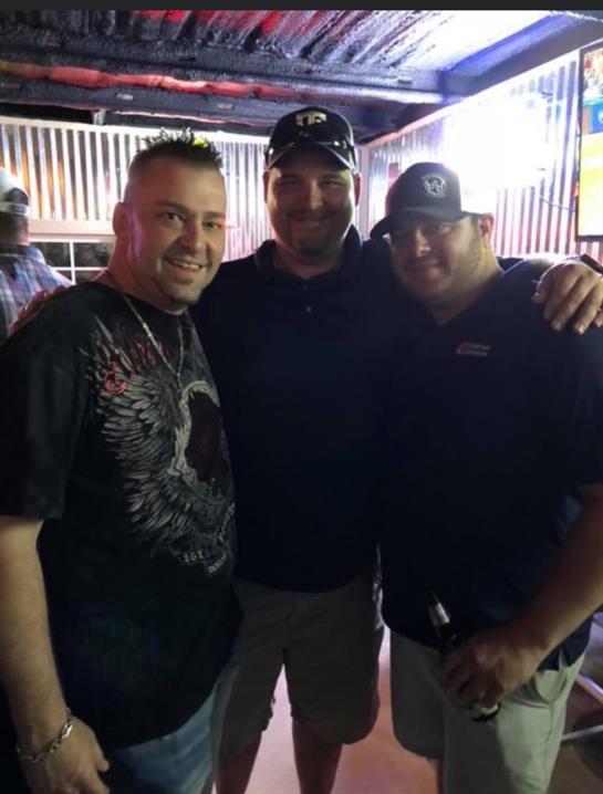 Three men pose together, smiling and enjoying their night at a vibrant local gathering place.