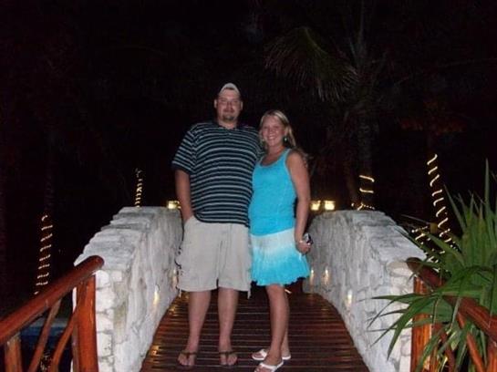 Happy couple poses together on a charming bridge surrounded by plants at night.