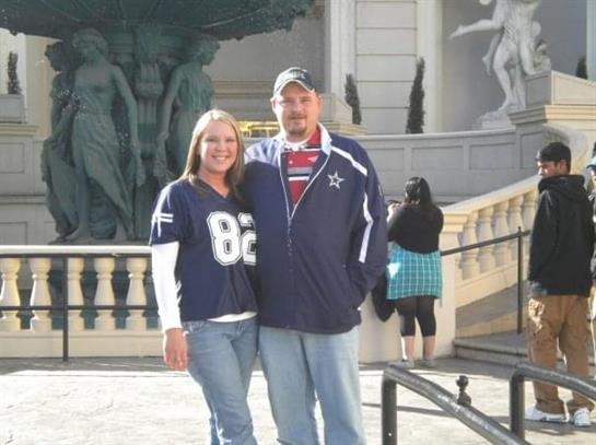 Happy couple stands side by side wearing sports jerseys and smiles in a lively outdoor area.