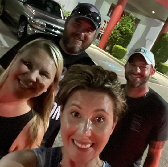 Friends gather outside a restaurant at night, smiling and posing for a cheerful selfie together.