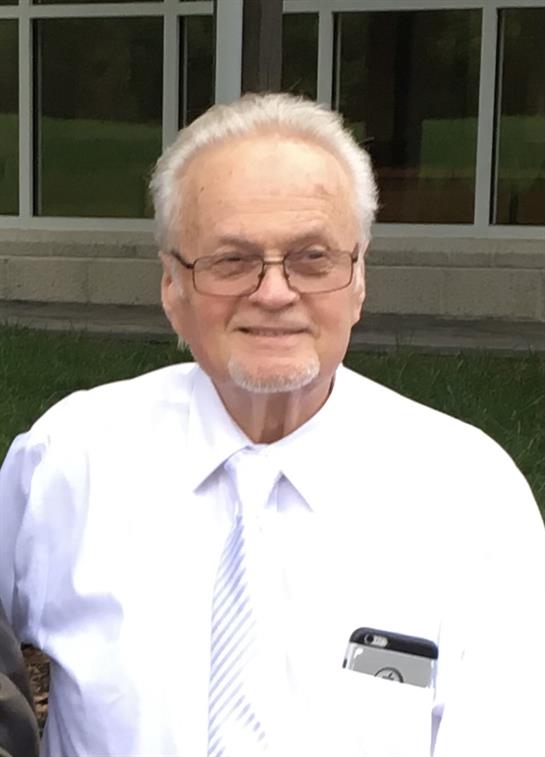 An elderly man in a white shirt and tie smiles at a friendly outdoor event.