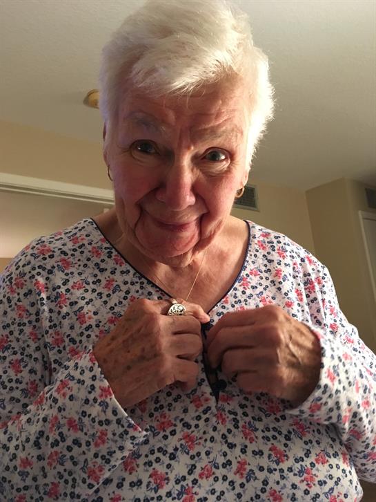 An elderly woman smiles while adjusting her top in a cozy home setting during the day.