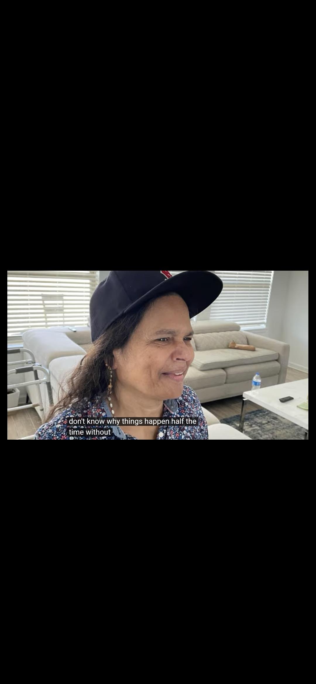 A woman with a baseball cap smiles while discussing her thoughts in a cozy living area.