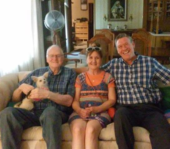 Four people sit comfortably on a couch, smiling together in a warm living area.