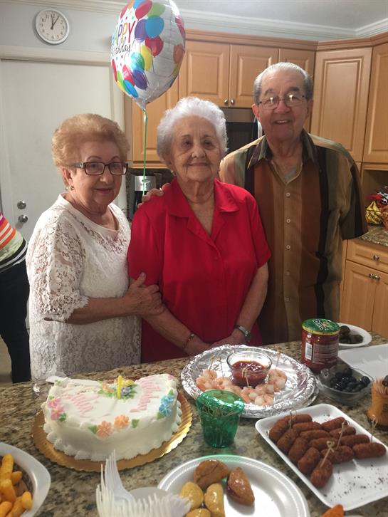 Three elderly individuals gather joyfully around a decorated table filled with food.