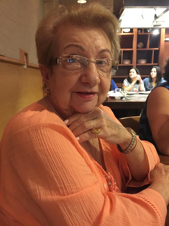 A cheerful elderly woman sits at a restaurant table during lunch with friends around her.