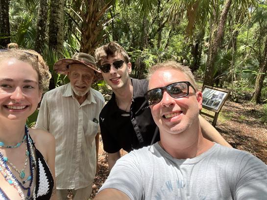 Four friends take a cheerful selfie while exploring a vibrant tropical forest.