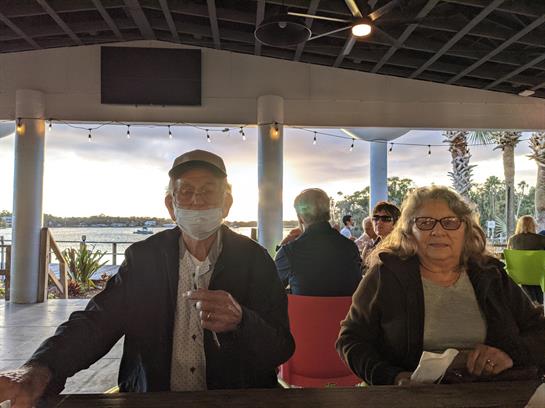 Two seniors relax at a cafe, sipping drinks and enjoying the sunset near the water.