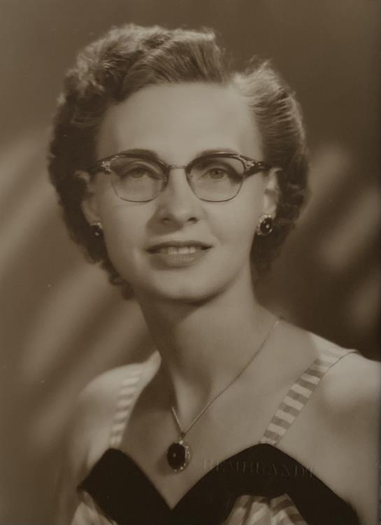 A vintage portrait captures a woman with glasses wearing a classy outfit and smiling warmly.